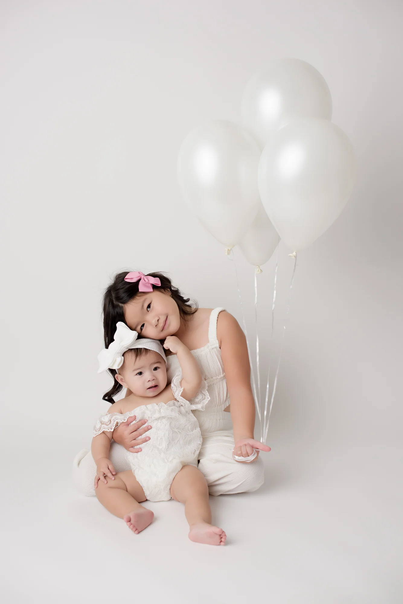 big sister holding white balloons and younger sister