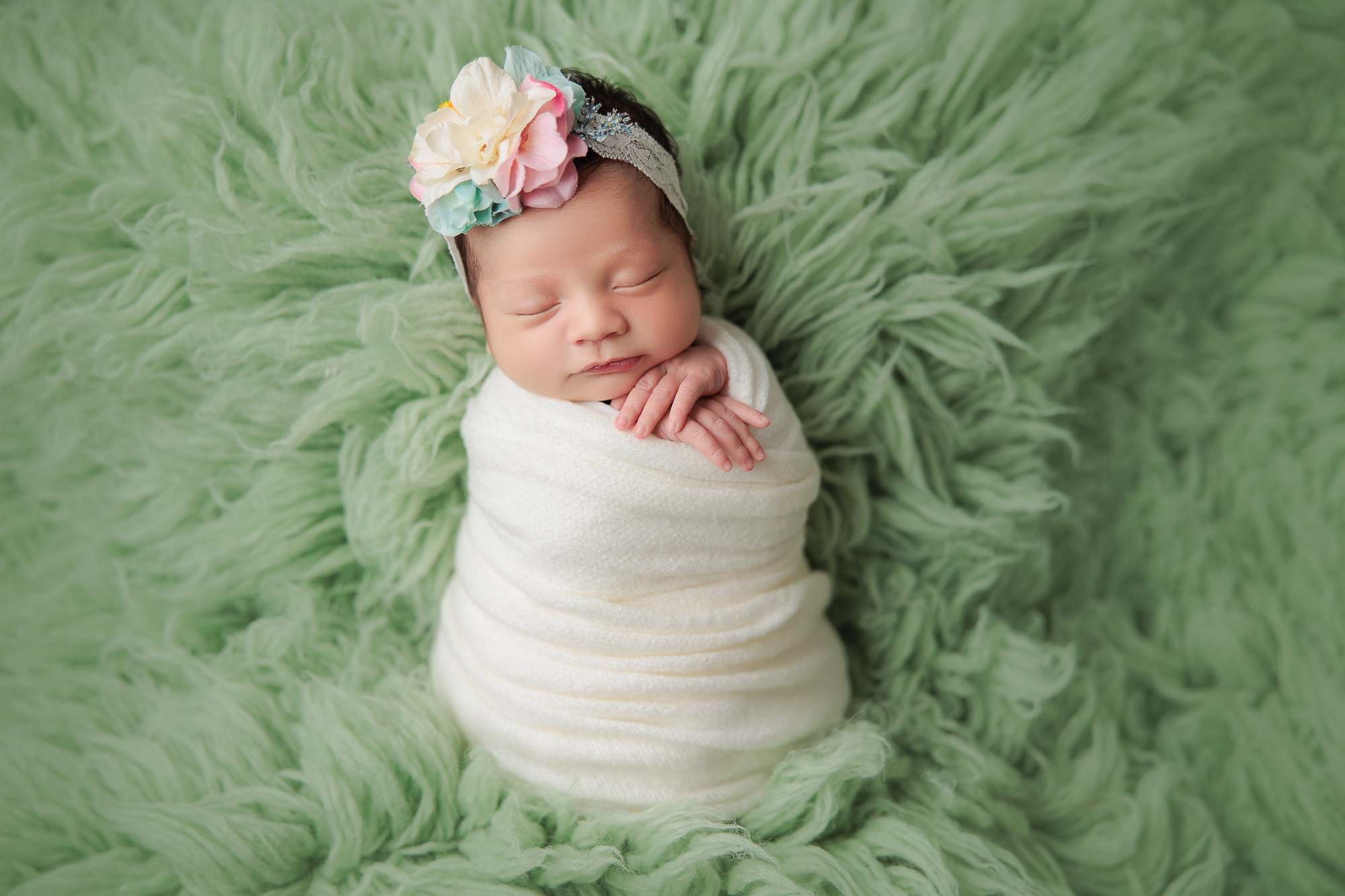 newborn photography amanda dams baby girl wearing flower headband on a green flokati