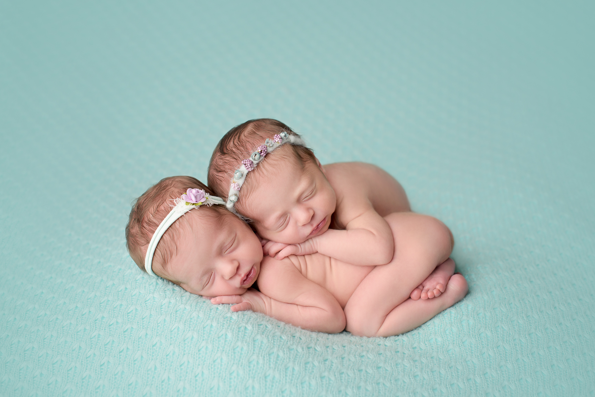 newborn photography of twin girls sleeping on a mint blanket