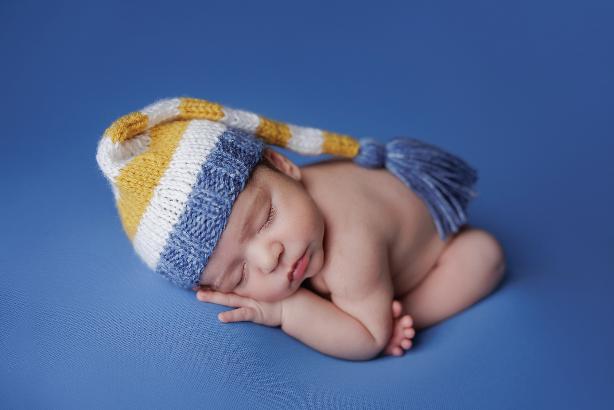 newborn photography by amanda dams - baby wearing a hat on blue backdrop