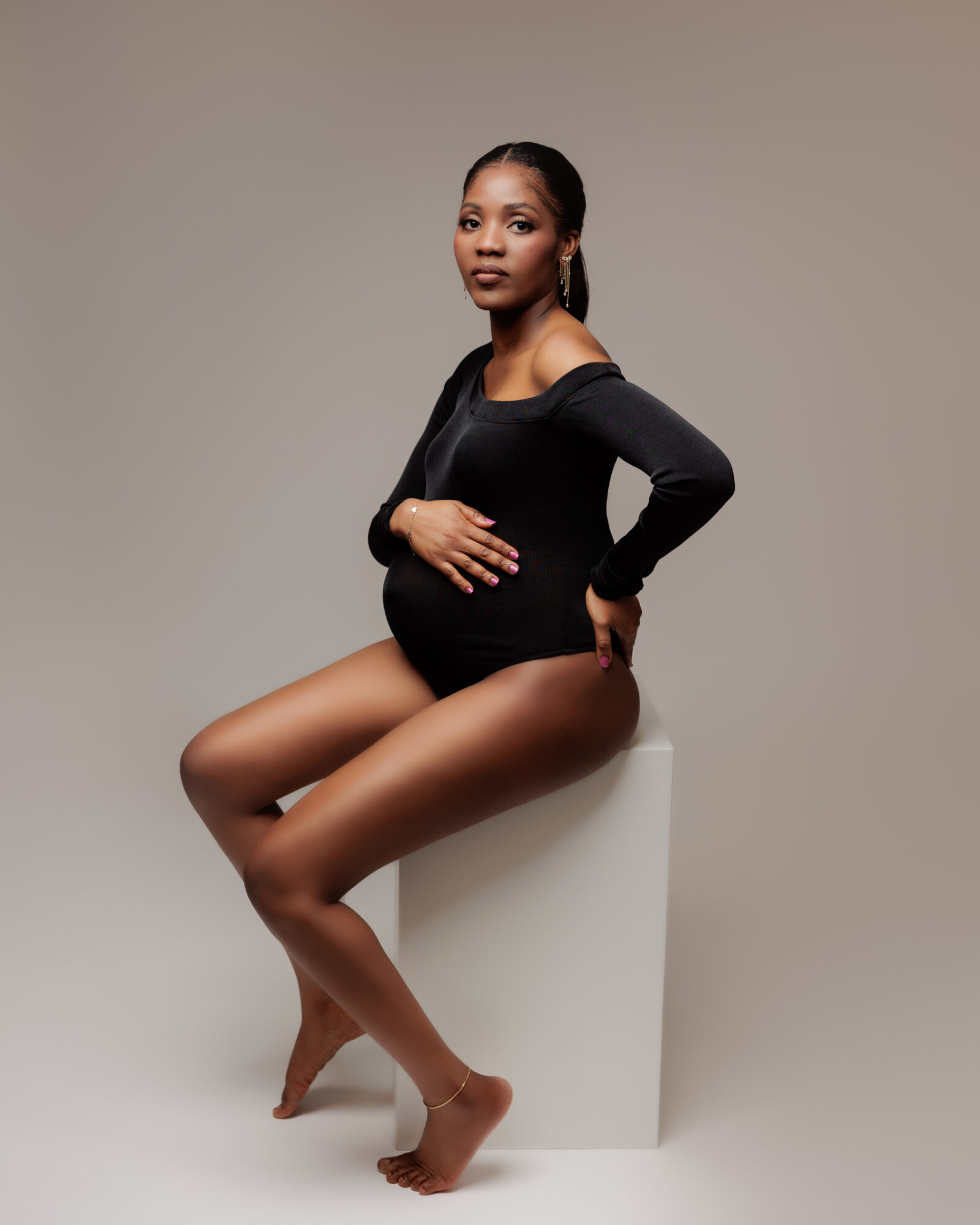 Amanda Dams Photography Maternity Seyi 2 Amanda Dams is a Calgary based Maternity Photographer. Shoot of a pregnant woman sitting on white box looking at the camera