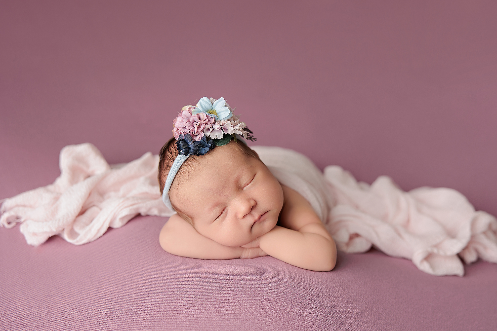 newborn baby sleeping on pink blanket wearing a flower headband